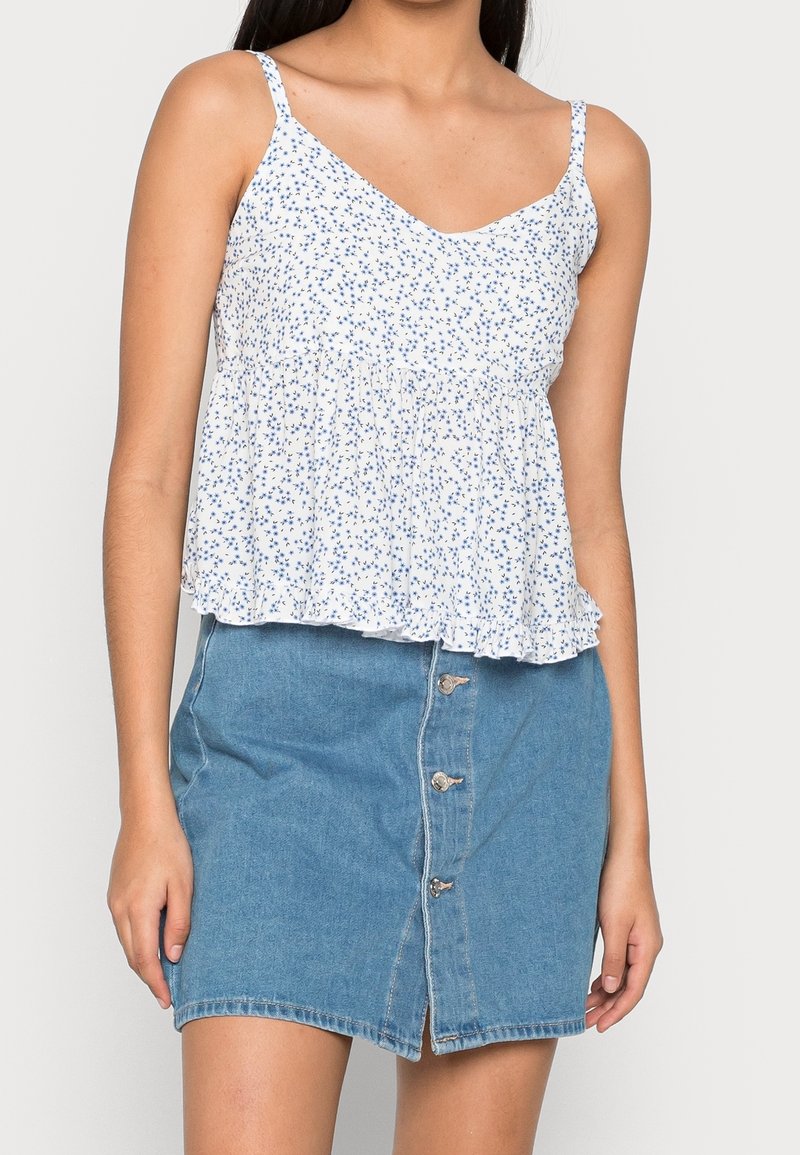 Vit blommig topp med V-ringning och justerbara band, tillsammans med en ljusblå denimkjol med knappfront och en lätt slits.