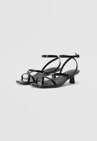 Sandales en cuir verni noir avec un bout carré, plusieurs fines lanières et un design à petit talon carré. Sangle simple à la cheville pour un maintien sécurisé.