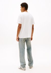 Camiseta blanca de algodón con mangas cortas, ajuste holgado, combinada con jeans de color azul claro y zapatillas negras y blancas. Atuendo simple y casual.