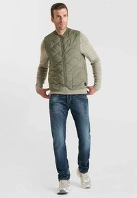 Groene, gewatteerde vest met een ronde hals, rits aan de voorkant en horizontale stiksels. Gecombineerd met donkerblauwe jeans en lichte sneakers.