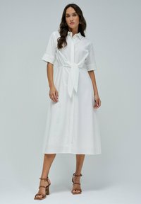 Abito camicia bianco con maniche corte, dettaglio della cintura legata in vita e orlo fino al ginocchio. Tessuto liscio, design con colletto e stile minimalista.