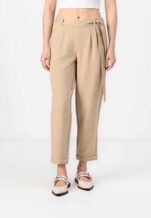 Beige høydejusterte bukser med folder, en knyttet belte og rullede mansjetter. Båret med lyse, blanke flats med stropp.