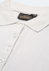 Weißes Poloshirt mit drei durchscheinenden weißen Knöpfen und einem schwarzen Etikett mit der Aufschrift "Switcher made with respect" an der Innenseite des Kragens.