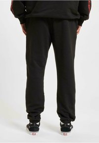 Sorte bomulls joggebukser med elastiske mansjetter, med en avslappet passform og subtil tekstur. Kombinert med svart og hvite sneakers.
