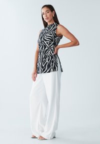 Mustvalge varrukateta topp sebratriipudega, kombineeritud lahtiste valgete pükstega. Sile kangapind ja vaba lõige.