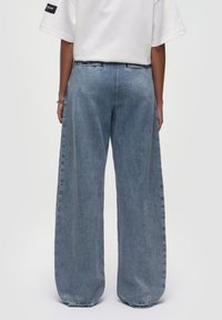 Pantalones vaqueros de pierna ancha en denim azul claro. Presentan una cintura alta, corte recto y un ligero desgastado. El dobladillo está ligeramente deshilachado, mostrando un estilo casual.