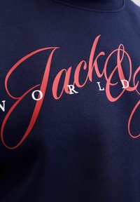 Sudadera navy con un texto en rojo y blanco en un estilo cursivo. La textura parece suave, con un cuello acanalado y sin adornos adicionales.
