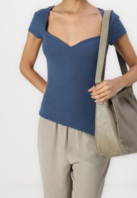 Námořnický pruhovaný top s hlubokým výstřihem do V a krátkými rukávy, v kombinaci se světlými béžovými širokými kalhotami a měkkou šedou kabelkou.