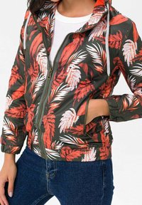 Tummanvihreä vetoketjullinen huppari, jossa on punavalkoisia trooppisia lehtikuvioita. Varustettu resorikahteilla hihansuissa ja etuvetoketjutaskulla.