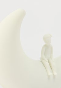 Λευκό διακοσμητικό γλυπτό σε σχήμα ημισελήνου με μια μικρή καθιστή φιγούρα στην άκρη του, και τα δύο κατασκευασμένα από λείο υλικό με ματ φινίρισμα.