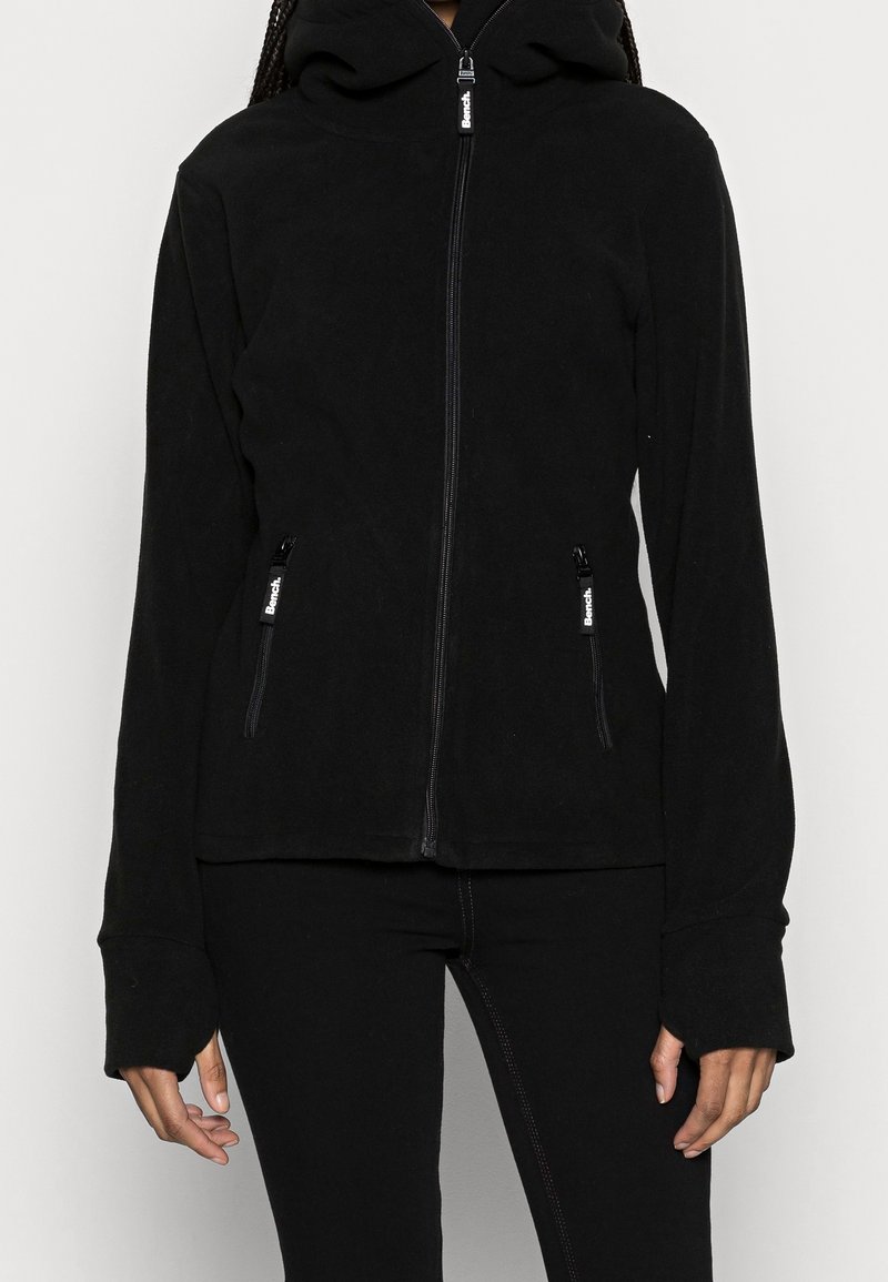 Zwarte fleecejack met een ritssluiting aan de voorkant, een capuchon, zijzakken en verlengde mouwen. Gladde textuur en minimalistisch ontwerp.