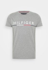 Grå kortärmad t-shirt med rund halsringning och texten "HILFIGER" samt ett horisontellt mönster i svart, vitt och rött över bröstet.