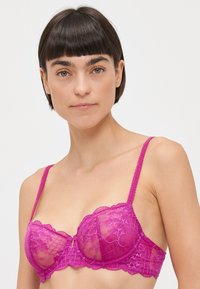 Pink lace bra with sheer cups and floral embroidery. Features adjustable straps and scalloped edges for a delicate design.
