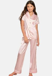 Rosa satinpyjamasset som består av en kortärmad knäppblus med en ficka och långa byxor med uppvikt fåll. Slät textur, glansig yta.