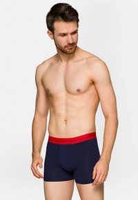Bokserki w granatowym kolorze z bawełny, z czerwoną elastyczną gumką z napisem "LANČERTO" w kolorze czarnym.