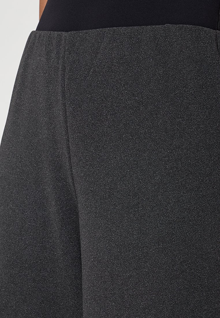Zwarte sportieve broek van een zacht, textuurstof, met een brede tailleband en een geheel aansluitende vorm. Subtiele glans zichtbaar op het oppervlak.