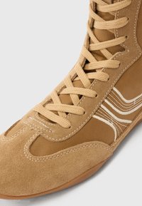 Tanni seemisnahast ja kangast toss, millel on kõrge sääreosa, kontrastsed valged triibud ning tekstuuriga paelad ja sile kummist tald.