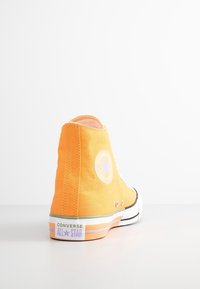 Une seule basket Converse All Star montante orange, tournée vers l’arrière sur une surface blanche, montrant le logo arrière et l’écusson latéral.