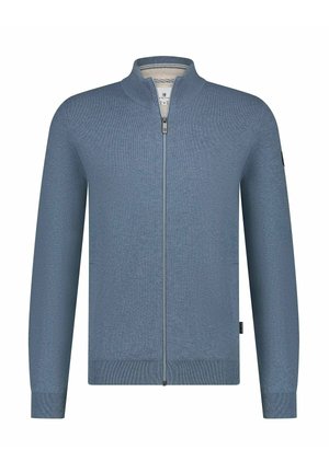 Man with light facial hair wearing a light blue ribbed high-collar sweater zipped to the top.