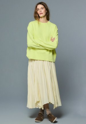 Laimeroheline ülegabariidiline dressipluus pikkade varrukatega, kombineeritud voolava helekollase plisseeritud seelikuga. Välimuse täiendavad pruunid tossud ja tekstuuriga kreemjad sokid.