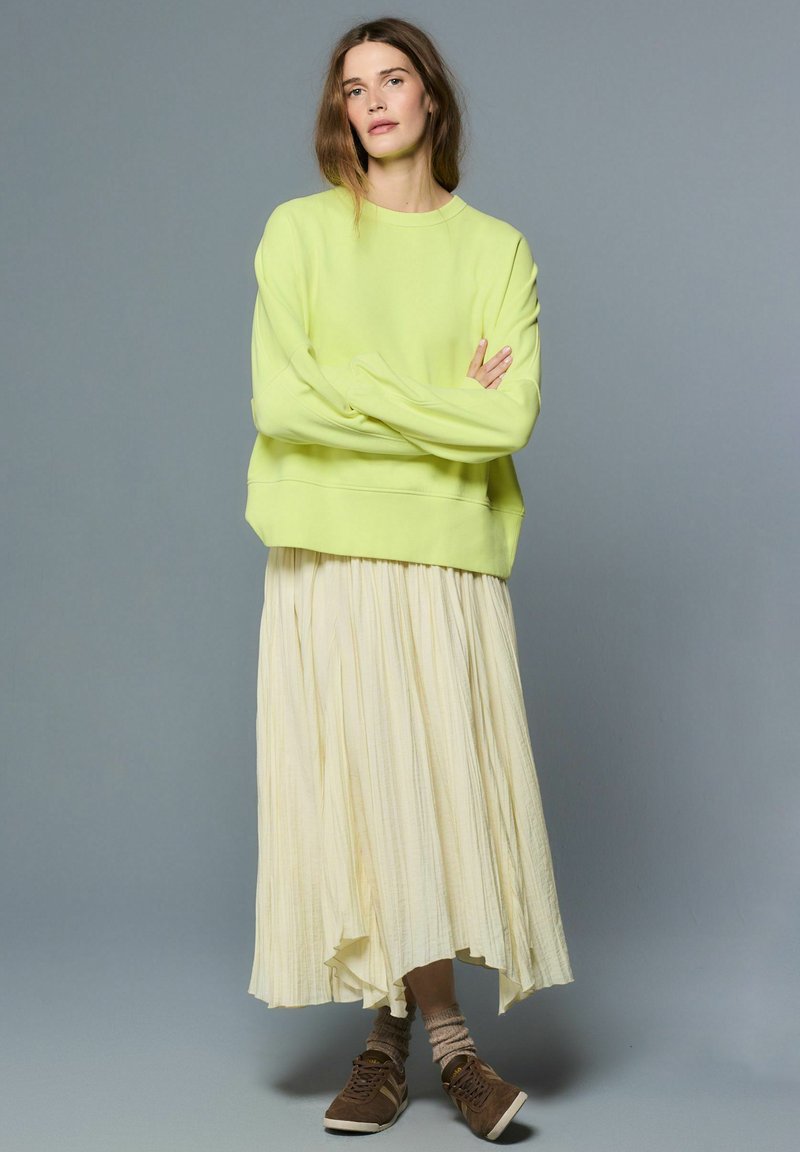 Prevelik svetlo zelena jopa z dolgimi rokavi, kombinirana z lahkotno svetlo rumeno nagubano krilo. Obleklo dopolnjujejo rjavi športni copati in teksturirane kremne nogavice.