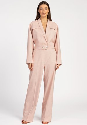 Lichtroze jumpsuit met lange mouwen, kraag, twee borstzakken en dubbele knoopsluiting bij de taille; wijde pijpenstijl met een gestructureerde stof.