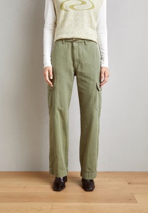 Pantalones cargo de color verde oliva con bolsillos laterales, un corte relajado y cierre de botón. Combinados con una blusa de manga larga de color claro.