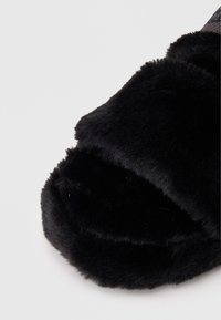 Schwarze flauschige Hausschuhe mit einer weichen, plüschigen Textur und einem breiten oberen Riemen, entworfen für Komfort und Wärme.