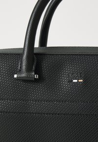 Borsa a tracolla in pelle nera con manici arrotondati, dotata di accessori in argento e logo. Caratteristico motivo impresso sulla superficie.
