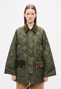 Zöld steppelt dzseki bársonyos, sötétzöld gallérral, oldalzsebekkel és arany színű fém részletekkel. Cipzáras záródású és laza szabású.