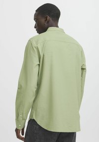Camicia a maniche lunghe verde chiaro realizzata in tessuto testurizzato, con polsini abbottonati e orlo curvo, dotata di colletto standard e dettagli sul giromanica.