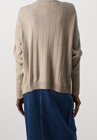 Beige ribattu pulloveri, jossa on rento istuvuus, pitkät hihat ja pyöristetty helma, yhdistettynä tummansiniseen farkkuhameeseen.