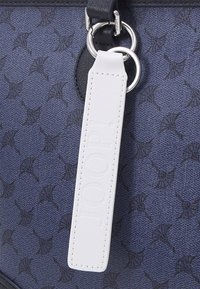 Sac à motifs bleus en tissu texturé, avec une étiquette en cuir blanc affichant "JOOP!" attachée par un anneau en argent.