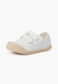 Baskets en toile blanches avec semelle en caoutchouc beige, équipées de deux bandes Velcro et d'une pointe arrondie pour un enfilage facile et un ajustement confortable.