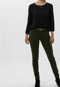 Top negro de manga larga con un escote redondo combinado con pantalones ajustados verde oliva. Los pantalones incluyen un cinturón con una hebilla plateada y bolsillos.