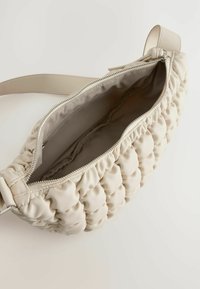 Beige quiltet håndtaske med en glat tekstur, en lynlåslukning og en justerbar rem. Indersiden er foret med et lysere stof.