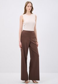 Top beige senza maniche abbinato a pantaloni brown a gamba larga e a vita alta. Tessuto liscio, cuciture minime, tessuto leggero e caduta morbida.