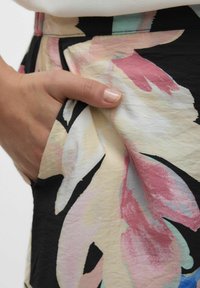 Bloemmotief stof in tinten roze, crème en zwart. Heeft een zakdetail en een lichte, gestructureerde stof.