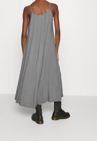 Grå ärmlös maxiklänning med sammanknutet bakdetalj, tillverkad av mjukt tyg. Matchad med svarta snörade kängor.