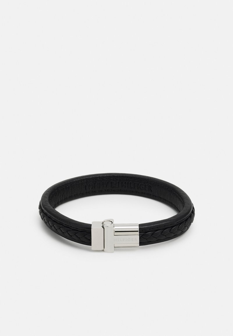 Pulseira de pele preta com padrão trançado, apresentando um fecho de metal prateado e logotipo em relevo. Textura suave, forma arredondada.
