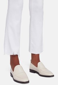 Mocassins en cuir blanc avec un bout arrondi et un minimum de couture, associés à un jean blanc avec un ourlet effiloché.