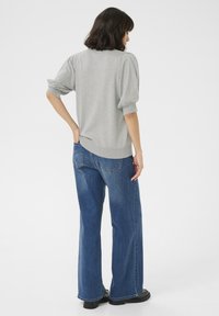 Pull gris avec des manches courtes froncées, associé à un jean bleu large. Texture lisse et coupe décontractée.