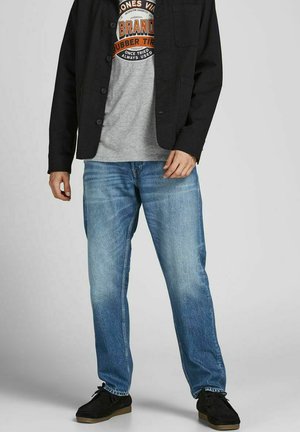 Mørk skjortebluse over en grå t-shirt med grafik, parret med lyseblå lige bukser og sorte sko.