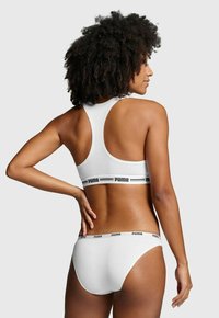 Weißes Sport-BH- und Bikini-Set mit schwarzem Puma-Logo am Band. Der Stoff wirkt glatt und hat ein einfaches Design.