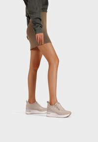 Sneaker beige con tomaia texturizzata, chiusura con lacci e suola bianca a contrasto. Presenta un logo sottile e dettagli accentuati.