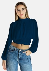 Cropped top blu navy con maniche lunghe e dettagli arricciati in vita, abbinato a jeans in denim leggeri a vita alta di colore blu chiaro.