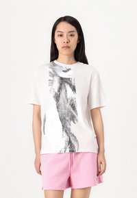 Hvid t-shirt med et stort, sølvfarvet abstrakt design, korte ærmer, rund hals. Sammen med lyserøde shorts med elastisk talje og snørresystem.