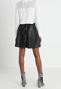 Jupe en cuir noir à coupe évasée, associée à un pull en maille blanche avec un dos texturé et des bottines grises à carreaux ornées de détails floraux.