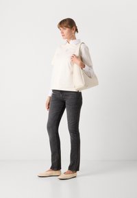 Top oversize beige chiaro con maniche corte, sovrapposto a una camicia bianca, abbinato a jeans grigio scuro e ballerine beige chiare. Borsa a spalla bianca.