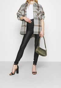 Gray plaid oversized shirt, white top, black faux leather pants, black strappy heels, and olive green handbag. Smooth textures and vibrant patterns.